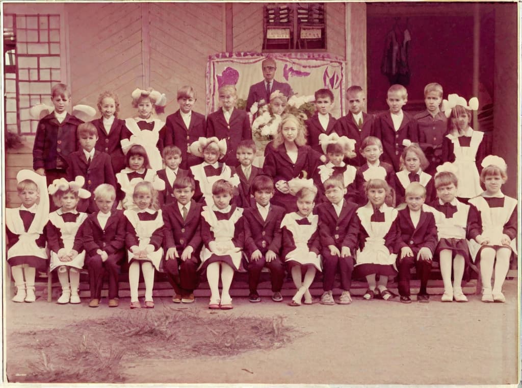  This photo was taken on September 1st 1986, exactly 128 days, or 4 months and 4 days, after the Chernobyl catastrophe took place. It captures my first day at in Gomel, Belarus. I had just turned that summer. In the photo, one can see my clmates and our teacher. Some are standing with their arms hanging beside their bodies, while others are seated on a low bench with their hands neatly placed on their . The students are arranged in three lines: 10 in the 3rd (top) back line, 9 in the 2nd (middle) line, and 13 in the 1st front line, totaling 32 students. There are 17 boys and 15 s, distinguished by the dress code. My friend Genadi is 4th from the right in the 3rd (top) line. I am seated in the very center of the