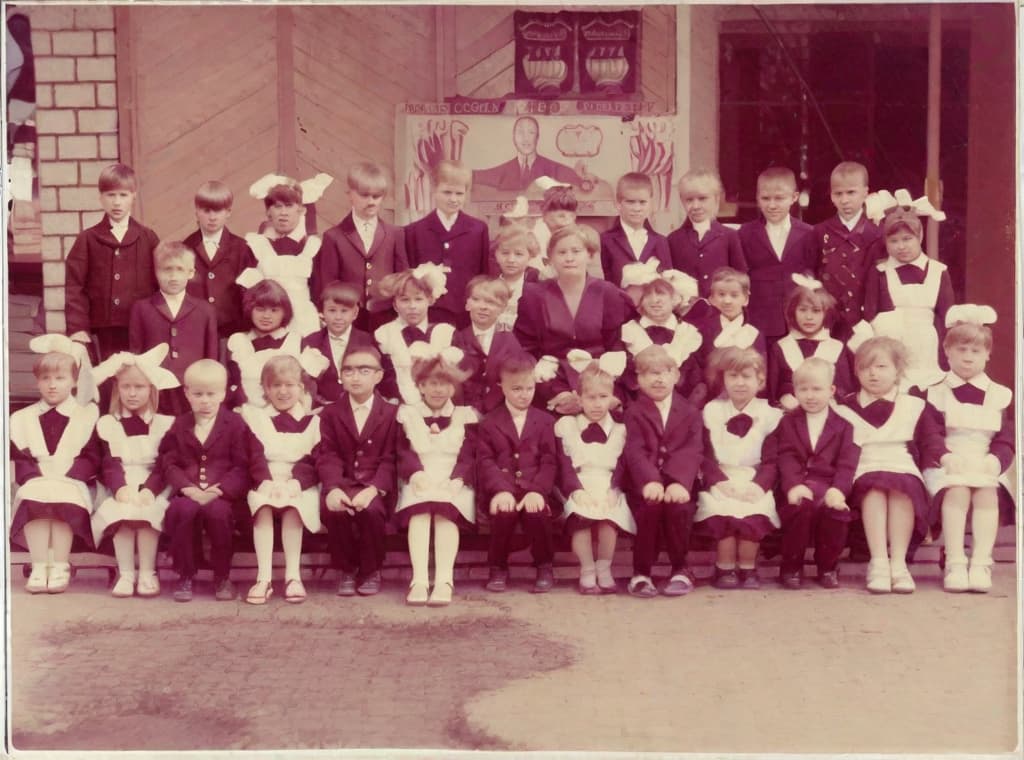  This photo was taken on September 1st 1986, exactly 128 days, or 4 months and 4 days, after the Chernobyl catastrophe took place. It captures my first day at in Gomel, Belarus. I had just turned that summer. In the photo, one can see my clmates and our teacher. Some are standing with their arms hanging beside their bodies, while others are seated on a low bench with their hands neatly placed on their . The students are arranged in three lines: 10 in the 3rd (top) back line, 9 in the 2nd (middle) line, and 13 in the 1st front line, totaling 32 students. There are 17 boys and 15 s, distinguished by the dress code. My friend Genadi is 4th from the right in the 3rd (top) line. I am seated in the very center of the