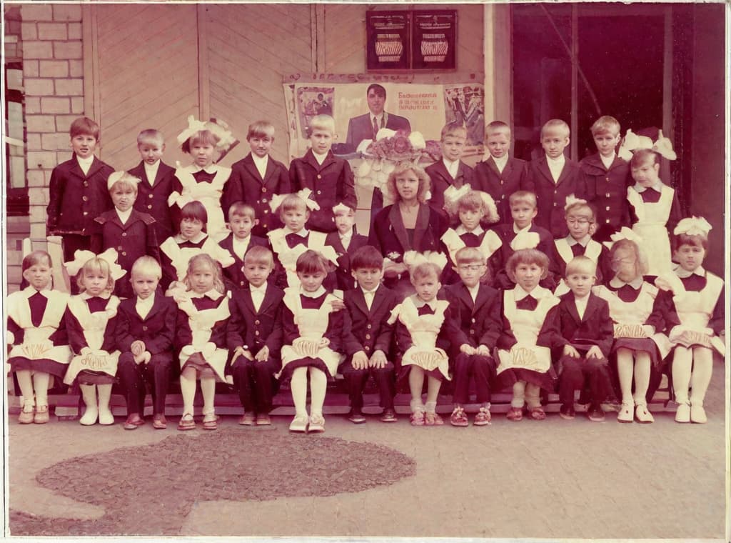  This photo was taken on September 1st 1986, exactly 128 days, or 4 months and 4 days, after the Chernobyl catastrophe took place. It captures my first day at in Gomel, Belarus. I had just turned that summer. In the photo, one can see my clmates and our teacher. Some are standing with their arms hanging beside their bodies, while others are seated on a low bench with their hands neatly placed on their . The students are arranged in three lines: 10 in the 3rd (top) back line, 9 in the 2nd (middle) line, and 13 in the 1st front line, totaling 32 students. There are 17 boys and 15 s, distinguished by the dress code. My friend Genadi is 4th from the right in the 3rd (top) line. I am seated in the very center of the