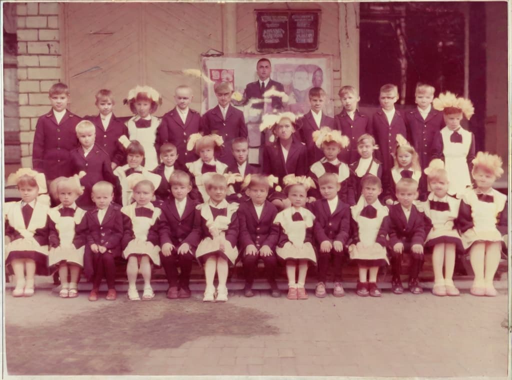  nine hundred and twenty eight days or four months and four days after the Chernobyl catastrophe took place. It captures my first day in Gomel, Belarus. I had just turned seven year that summer. In this photo, one can see my clmates. and our teacher. Some are standing with their arms hanging besides their bodies while others are seated on the on on the low bench with with our hands neatly placed on their . The students are arranged in three lines, ten in the third top back line, three. 9 in the second middle line and 13 in the first front line, totally in 13. There are 17 boys and 15 s distinguished by the dress code. My friend Gennady is the fourth from the right on the third top line.;