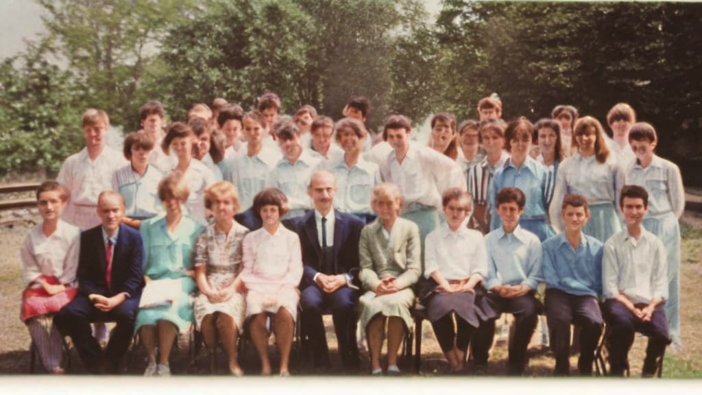  This photo was taken on September 1st 1986, exactly 128 days, or 4 months and 4 days, after the Chernobyl catastrophe took place. It captures my first day at in Gomel, Belarus. I had just turned that summer. In the photo, one can see my clmates and our teacher. Some are standing with their arms hanging beside their bodies, while others are seated on a low bench with their hands neatly placed on their . The students are arranged in three lines: 10 in the 3rd (top) back line, 9 in the 2nd (middle) line, and 13 in the 1st front line, totaling 32 students. There are 17 boys and 15 s, distinguished by the dress code. My friend Genadi is 4th from the right in the 3rd (top) line. I am seated in the very center of the