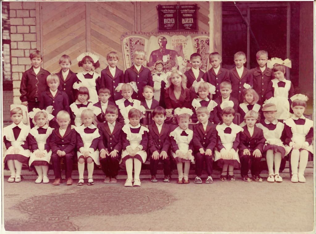  This photo was taken on September 1st 1986, exactly 128 days, or 4 months and 4 days, after the Chernobyl catastrophe took place. It captures my first day at in Gomel, Belarus. I had just turned that summer. In the photo, one can see my clmates and our teacher. Some are standing with their arms hanging beside their bodies, while others are seated on a low bench with their hands neatly placed on their . The students are arranged in three lines: 10 in the 3rd (top) back line, 9 in the 2nd (middle) line, and 13 in the 1st front line, totaling 32 students. There are 17 boys and 15 s, distinguished by the dress code. My friend Genadi is 4th from the right in the 3rd (top) line. I am seated in the very center of the