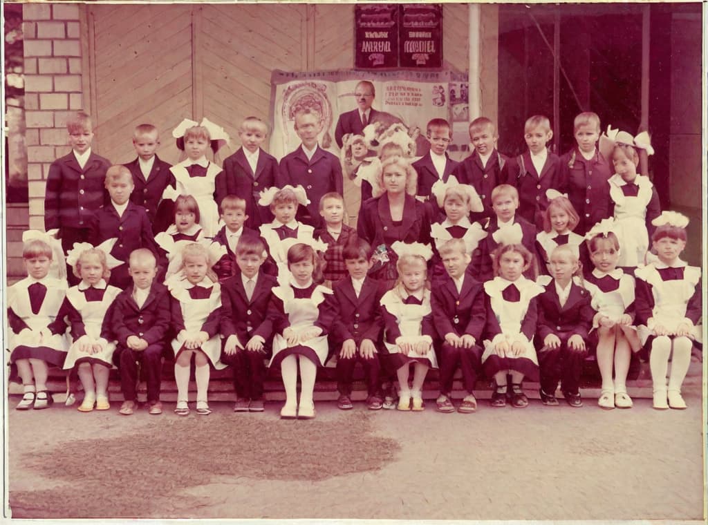  This photo was taken on September 1st 1986, exactly 128 days, or 4 months and 4 days, after the Chernobyl catastrophe took place. It captures my first day at in Gomel, Belarus. I had just turned that summer. In the photo, one can see my clmates and our teacher. Some are standing with their arms hanging beside their bodies, while others are seated on a low bench with their hands neatly placed on their . The students are arranged in three lines: 10 in the 3rd (top) back line, 9 in the 2nd (middle) line, and 13 in the 1st front line, totaling 32 students. There are 17 boys and 15 s, distinguished by the dress code. My friend Genadi is 4th from the right in the 3rd (top) line. I am seated in the very center of the