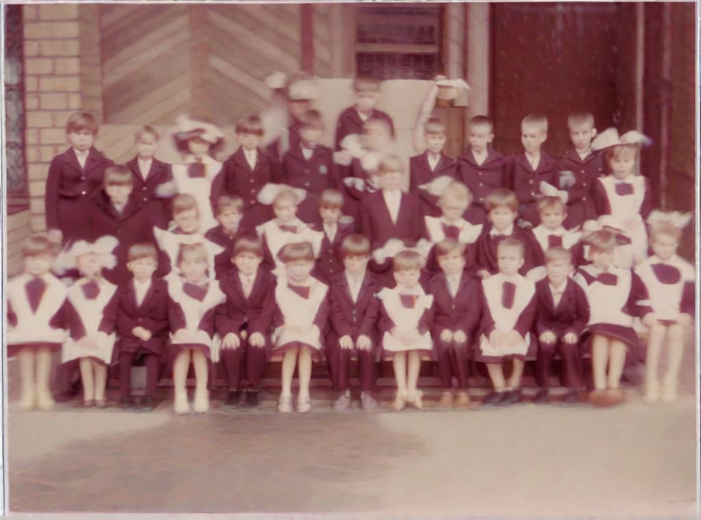  This photo was taken on September 1st 1986, exactly 128 days, or 4 months and 4 days, after the Chernobyl catastrophe took place. It captures my first day at in Gomel, Belarus. I had just turned that summer. In the photo, one can see my clmates and our teacher. Some are standing with their arms hanging beside their bodies, while others are seated on a low bench with their hands neatly placed on their . The students are arranged in three lines: 10 in the 3rd (top) back line, 9 in the 2nd (middle) line, and 13 in the 1st front line, totaling 32 students. There are 17 boys and 15 s, distinguished by the dress code. My friend Genadi is 4th from the right in the 3rd (top) line. I am seated in the very center of the