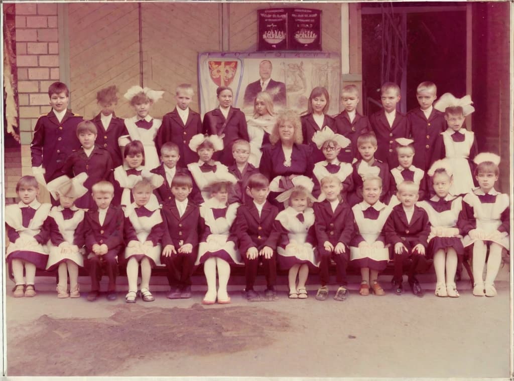  This photo was taken on September 1st 1986, exactly 128 days, or 4 months and 4 days, after the Chernobyl catastrophe took place. It captures my first day at in Gomel, Belarus. I had just turned that summer. In the photo, one can see my clmates and our teacher. Some are standing with their arms hanging beside their bodies, while others are seated on a low bench with their hands neatly placed on their . The students are arranged in three lines: 10 in the 3rd (top) back line, 9 in the 2nd (middle) line, and 13 in the 1st front line, totaling 32 students. There are 17 boys and 15 s, distinguished by the dress code. My friend Genadi is 4th from the right in the 3rd (top) line. I am seated in the very center of the