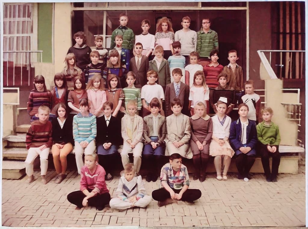  This photo was taken on September 1st 1986, exactly 128 days, or 4 months and 4 days, after the Chernobyl catastrophe took place. It captures my first day at in Gomel, Belarus. I had just turned that summer. In the photo, one can see my clmates and our teacher. Some are standing with their arms hanging beside their bodies, while others are seated on a low bench with their hands neatly placed on their . The students are arranged in three lines: 10 in the 3rd (top) back line, 9 in the 2nd (middle) line, and 13 in the 1st front line, totaling 32 students. There are 17 boys and 15 s, distinguished by the dress code. My friend Genadi is 4th from the right in the 3rd (top) line. I am seated in the very center of the