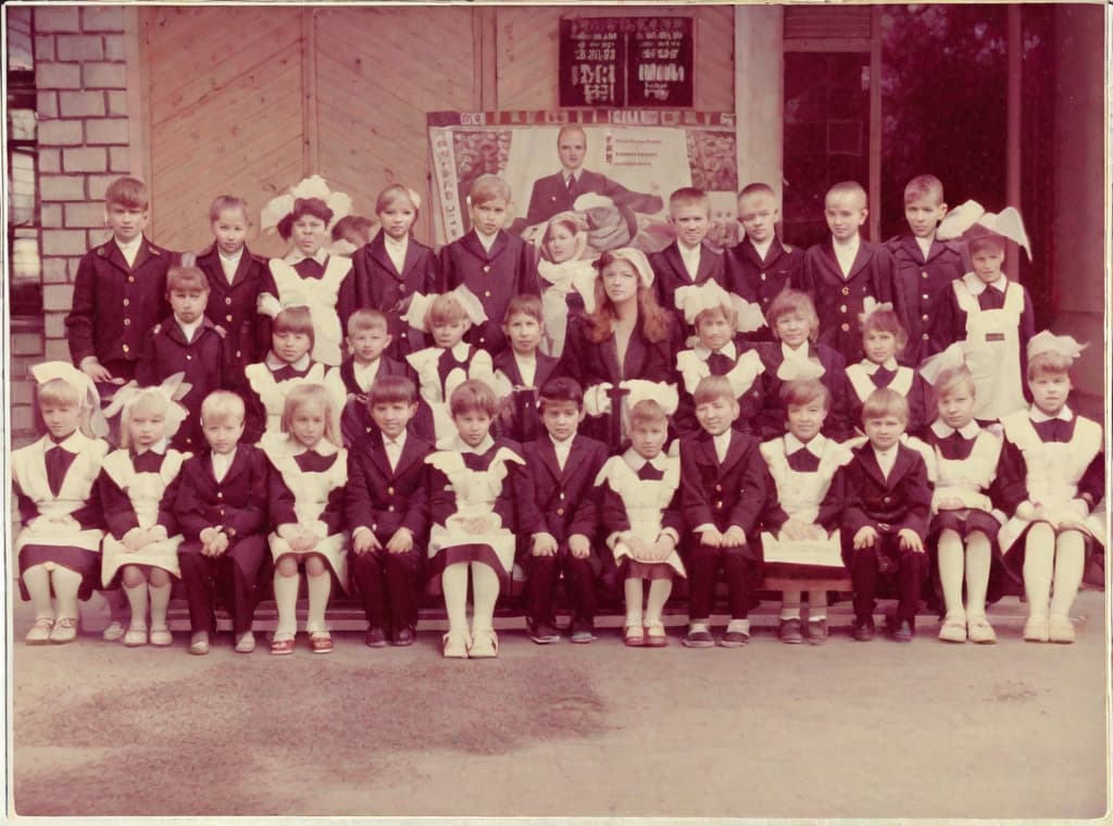  [BLANK AUDIO] This photo was taken on September 1st 1986, exactly 128 days or 4 months and 4 days. days after the Chernobyl catastrophe took place. It captures my first day at in Gomel, Belarus. We just turned that summer. In the photo one can see my clmates and our teacher. Some are standing with their eyes open. their arms hanging besides their bodies, while others are seated on a low bench with their hands neatly placed on their . The students are arranged in in three lines. Ten in the third top back line, nine in the second middle line and thir in the first front line. Totaling 32 students. There are 17 boys and 15 s distinguished by the dress code. My friend Gennady is fourth from the right on the thi