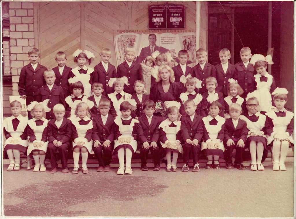  It was taken on September 1st 1986, exactly 128 days or 40 months and 4 days after the Chernobyl catastrophe took place. first day at in Gomel, Belarus. I had just turned seven year that summer. In the photo one can see my clmates. mates and our teacher. Some are standing with their arms hanging besides their bodies, while others are seated on a low bench with their hands neatly placed. placed on their . The students are arranged in three lines. Ten in the third top line, nine in the second middle line. the line and 13 in the first front line, totaling 32 students. There are 17 boys and 15 s. distinguished by the gr coat. My friend Gennady is the fourth from the right in the third top line. I am seated in the very