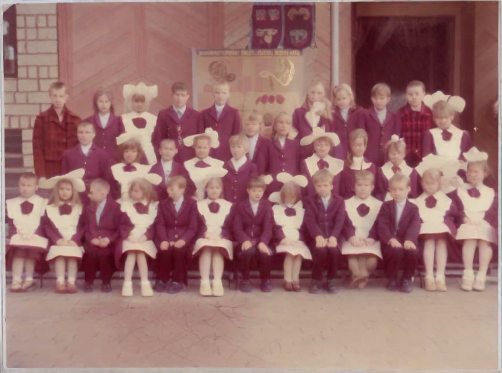  This photo was taken on September 1st 1986, exactly 128 days, or 4 months and 4 days, after the Chernobyl catastrophe took place. It captures my first day at in Gomel, Belarus. I had just turned that summer. In the photo, one can see my clmates and our teacher. Some are standing with their arms hanging beside their bodies, while others are seated on a low bench with their hands neatly placed on their . The students are arranged in three lines: 10 in the 3rd (top) back line, 9 in the 2nd (middle) line, and 13 in the 1st front line, totaling 32 students. There are 17 boys and 15 s, distinguished by the dress code. My friend Genadi is 4th from the right in the 3rd (top) line. I am seated in the very center of the