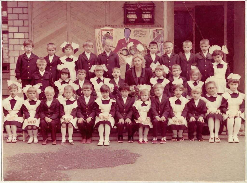  This photo was taken on September 1st 1986, exactly 128 days, or 4 months and 4 days, after the Chernobyl catastrophe took place. It captures my first day at in Gomel, Belarus. I had just turned that summer. In the photo, one can see my clmates and our teacher. Some are standing with their arms hanging beside their bodies, while others are seated on a low bench with their hands neatly placed on their . The students are arranged in three lines: 10 in the 3rd (top) back line, 9 in the 2nd (middle) line, and 13 in the 1st front line, totaling 32 students. There are 17 boys and 15 s, distinguished by the dress code. My friend Genadi is 4th from the right in the 3rd (top) line. I am seated in the very center of the