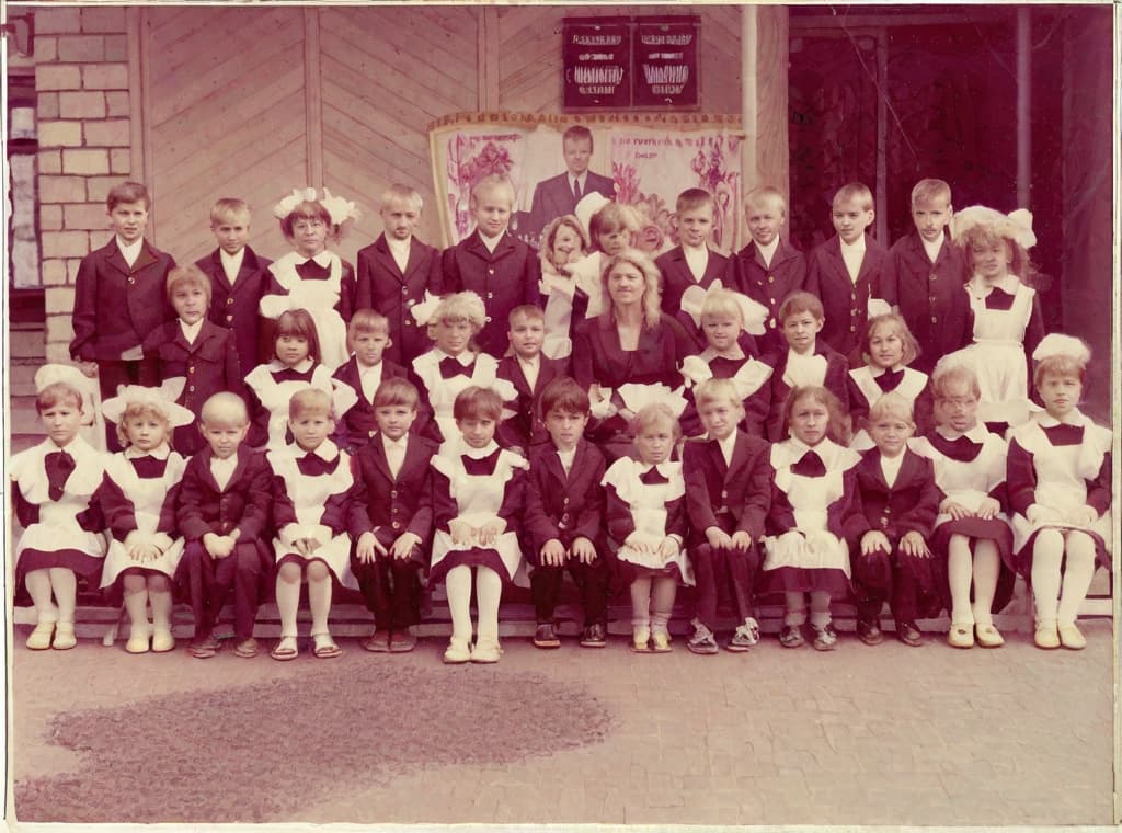  This photo was taken on September 1st 1986, exactly 128 days, or 4 months and 4 days, after the Chernobyl catastrophe took place. It captures my first day at in Gomel, Belarus. I had just turned that summer. In the photo, one can see my clmates and our teacher. Some are standing with their arms hanging beside their bodies, while others are seated on a low bench with their hands neatly placed on their . The students are arranged in three lines: 10 in the 3rd (top) back line, 9 in the 2nd (middle) line, and 13 in the 1st front line, totaling 32 students. There are 17 boys and 15 s, distinguished by the dress code. My friend Genadi is 4th from the right in the 3rd (top) line. I am seated in the very center of the