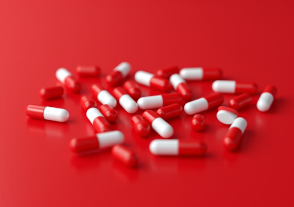  pile of glossy red and white capsule pills on a reflective red surface with a matching red background