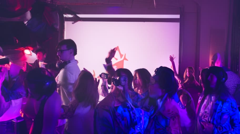  soviet style prom night party, set in the 1980s, with a dj booth in the center of the room. the dj is dressed in a pioneer uniform with square glasses, headphones, complete with a red tie and a enthusiastic expression. the room is filled with retro soviet decorations, including hammer and sickle symbols, soviet flags, and vintage posters. the walls and ceiling are adorned with neon lights, casting a colorful glow over the scene. the overall mood is one of nostalgia and joy, capturing the excitement and energy of a soviet era prom night.