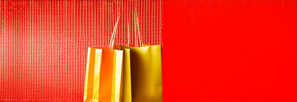  professional detailed photography, gold colored shopping bags on red shiny background on the right, empty space for text on the left, bokeh ar 3:1, (muted colors, dim colors, soothing tones), (vsco:0.3)