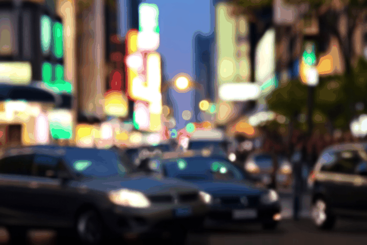 A bustling city street at dusk, cars and people moving in a lively rhythm as neon lights flicker to life. The camera zooms in on a lone figure walking with purpose